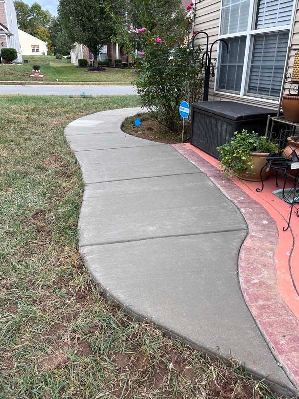 Gray concrete sidewalk curves through a grassy yard to a porch