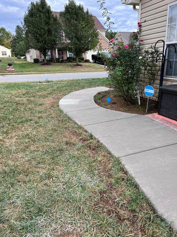 Concrete walkway curves past grass lawn, house with rose bush, and blue security sign