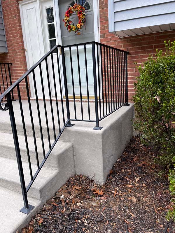 Black railing on concrete steps leading to a door with a wreath