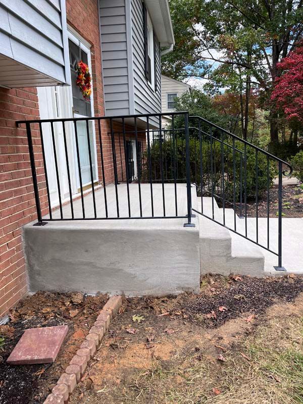 Black railing on concrete steps and porch of a two-story brick and gray-sided house