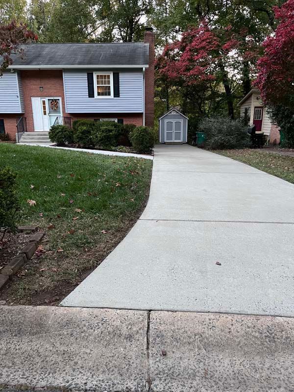 House with concrete driveway; shed in the background. Green grass and trees line the property.