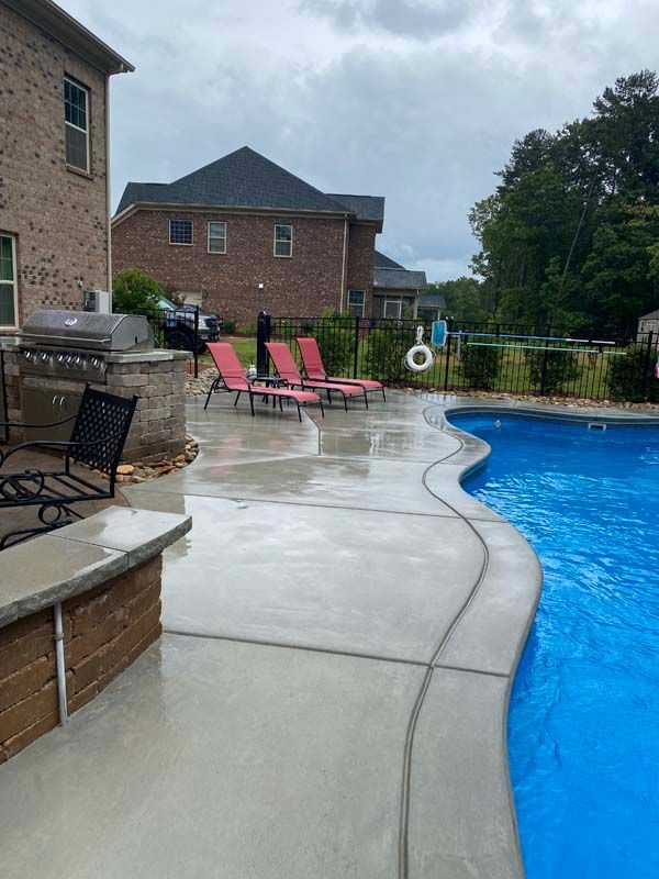Backyard with a pool, concrete patio, brick house, lounge chairs, and cloudy sky