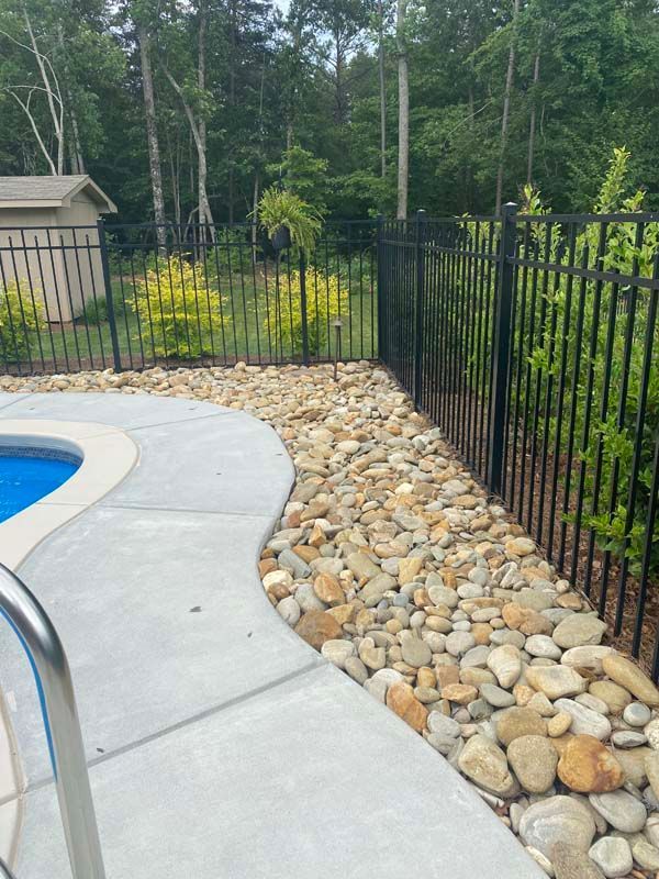 Poolside with concrete, rocks, black fence, and trees