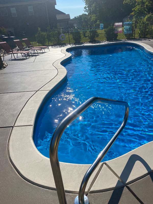 Pool with clear blue water, silver handrail, and concrete deck in sunny outdoor setting
