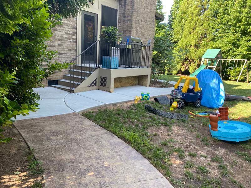 A concrete walkway leads to a house with a small porch, children's toys scattered on a grassy yard