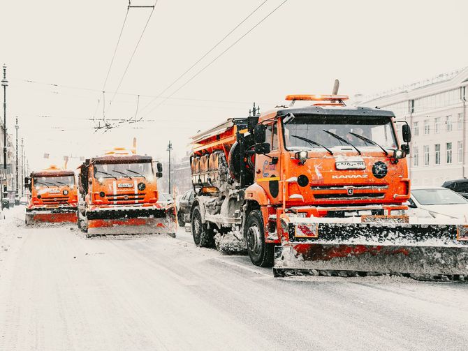 Orange snowplows clearing a snow-covered city street during heavy snowfall