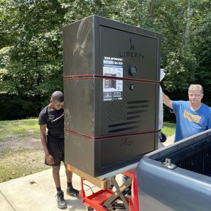 Two men loading a large black safe from a truck onto a lift outdoors.