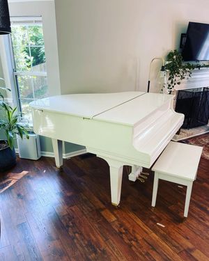 White grand piano with matching bench in a room with wood flooring, near a window and fireplace.