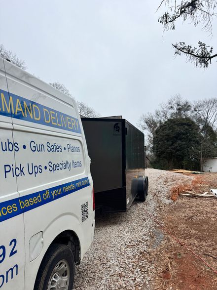 Van and trailer on a gravel driveway. Van has company logo. Cloudy sky, trees in the background.