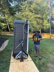 Man with thumbs up next to a hot tub on a pallet jack on a wooden ramp outdoors.
