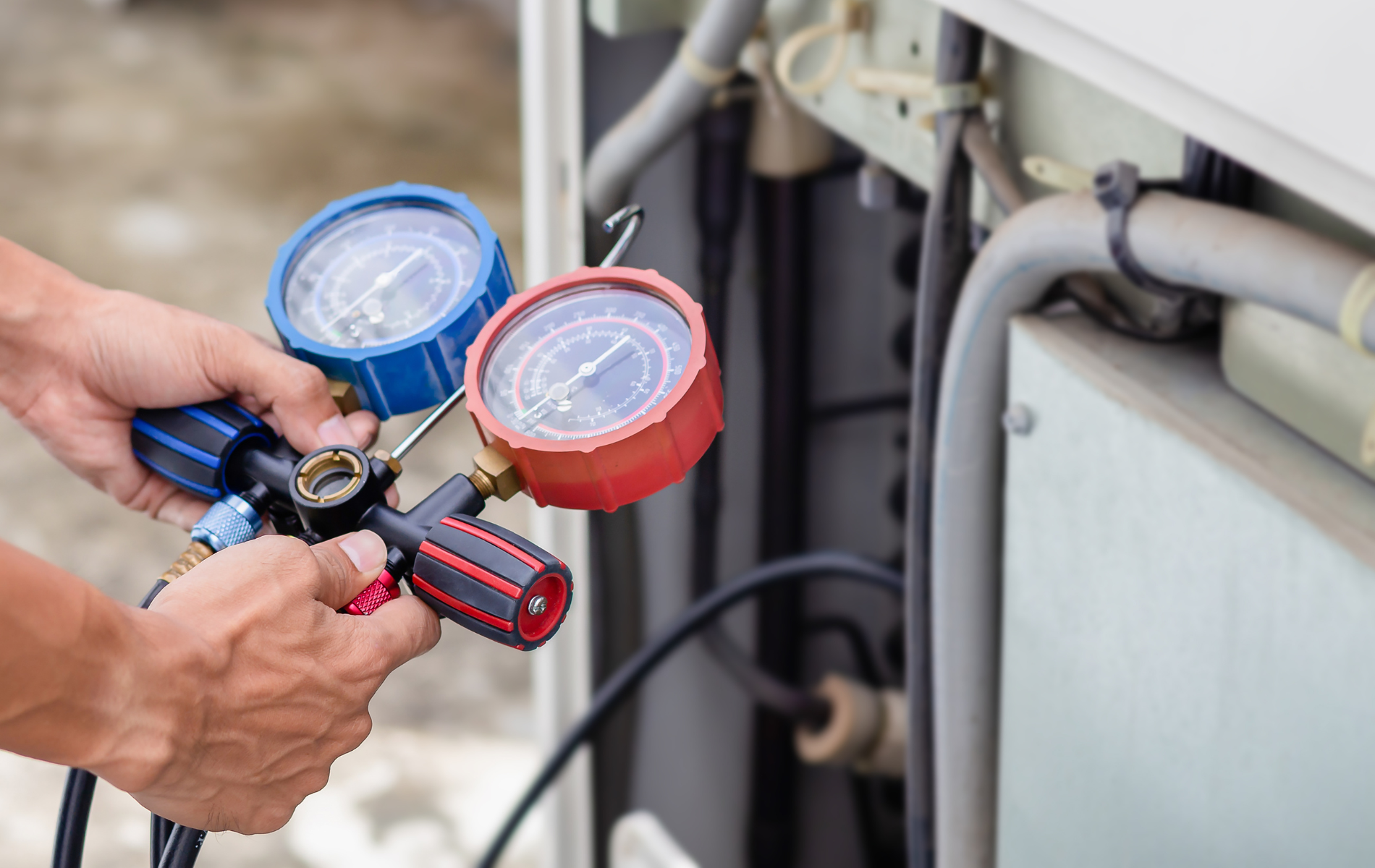 A man is holding two gauges in his hands while working on an air conditioner.