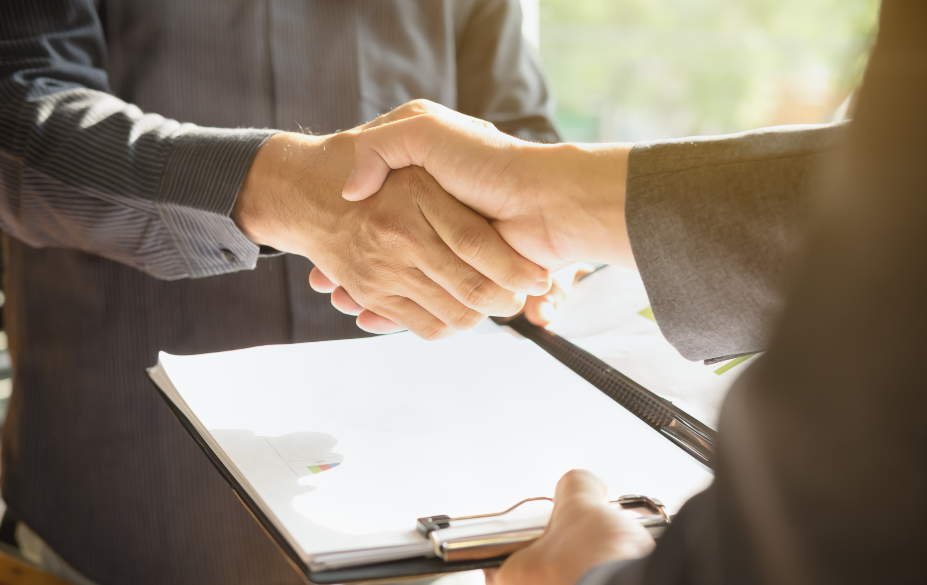 A man is shaking hands with another man while holding a clipboard.