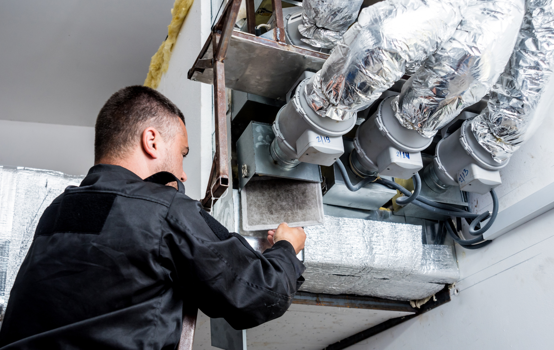 A man is working on a ventilation system in a building.