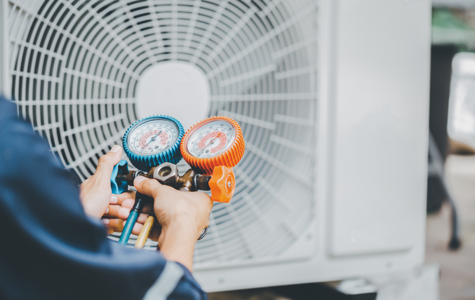 A man is working on an air conditioner with a pair of gauges.