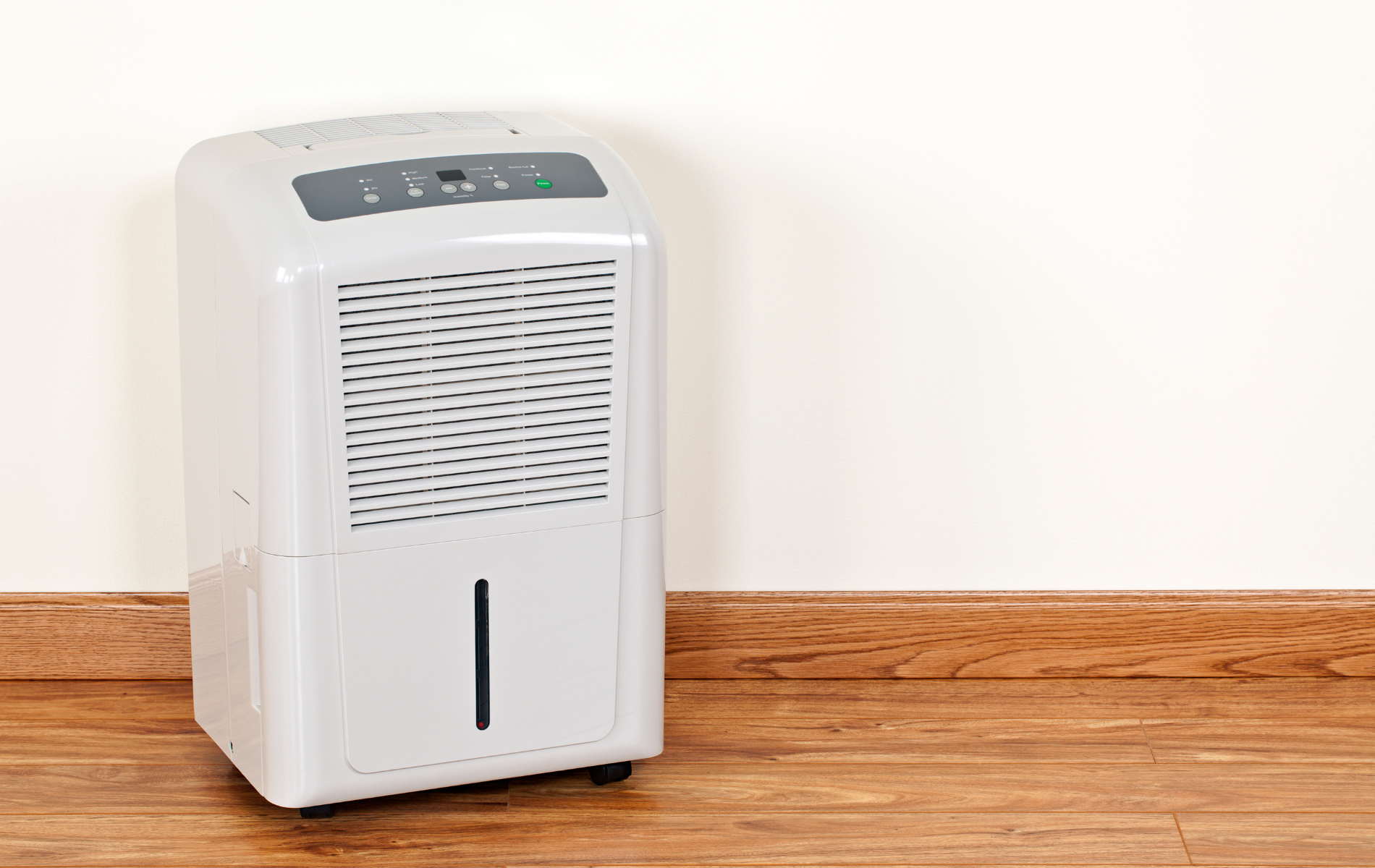 A white dehumidifier is sitting on a wooden floor next to a wall.