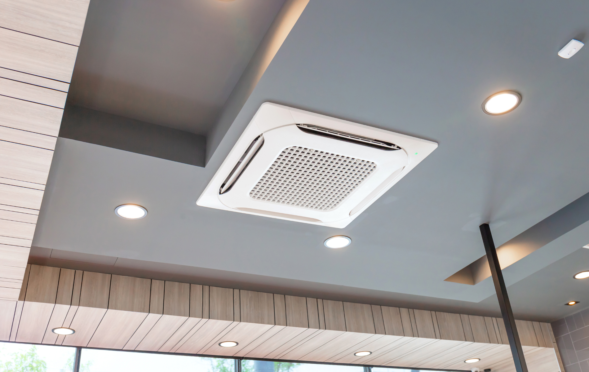 A square air conditioner is hanging from the ceiling of a room.