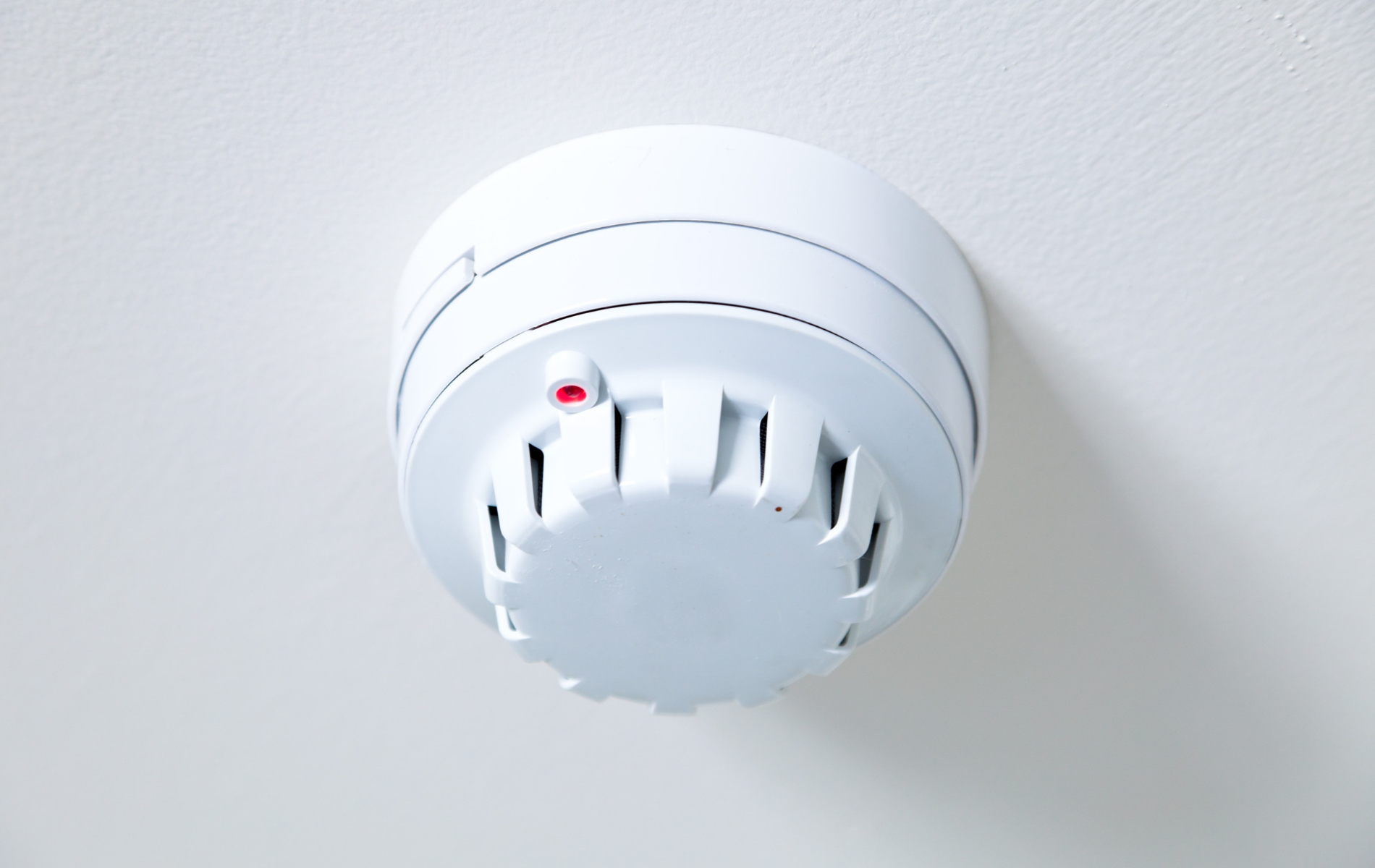 A white smoke detector is mounted on a white wall.