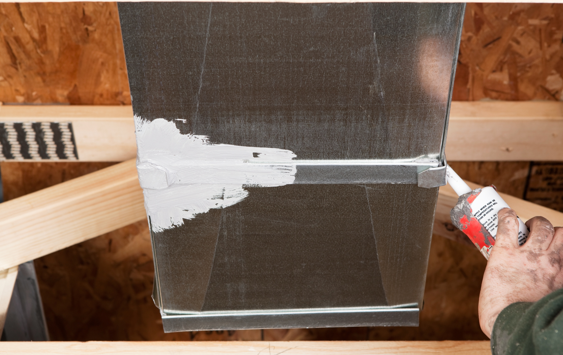 A person is applying silicone to a metal pipe.