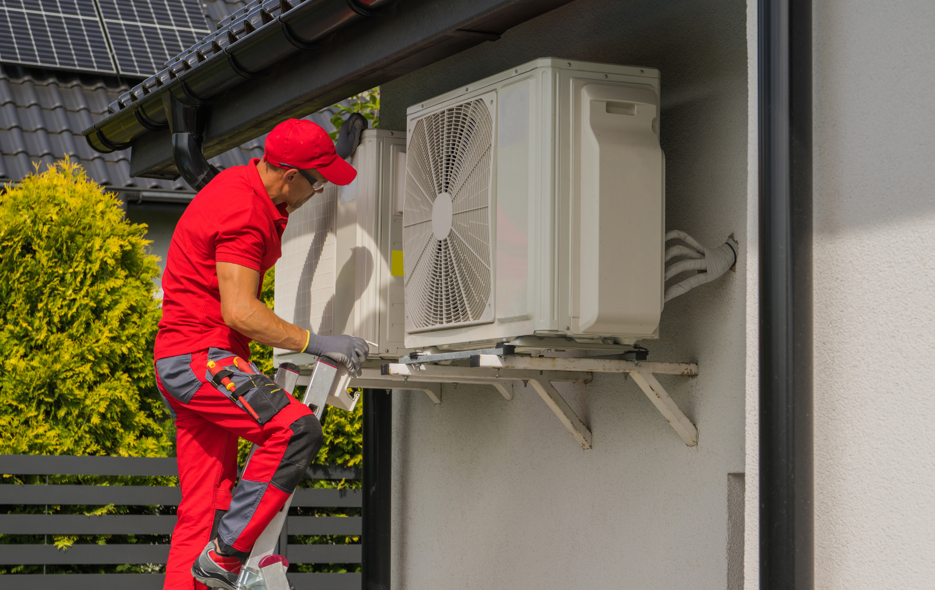 A man is installing an air conditioner on the side of a house.
