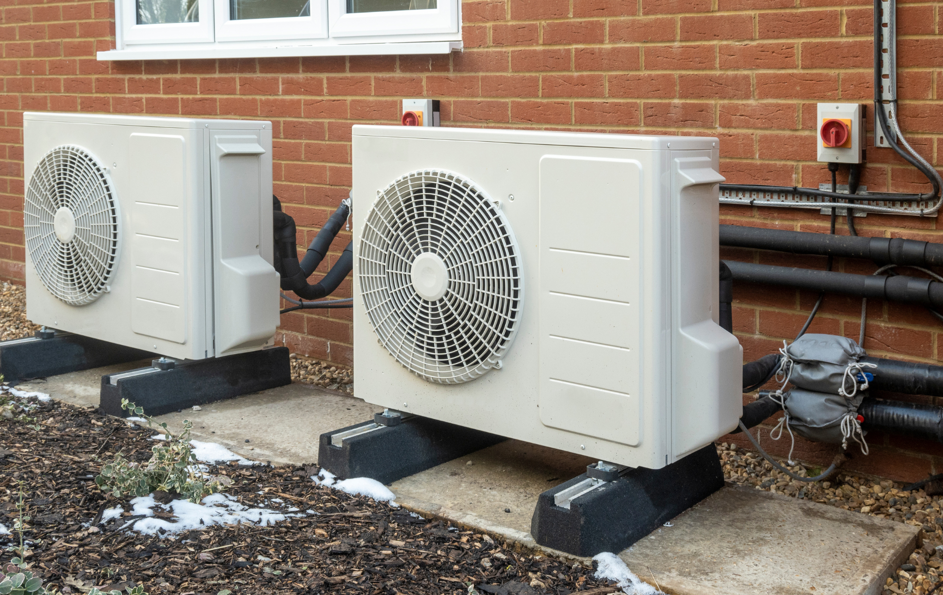 Two air conditioners are sitting outside of a brick building.