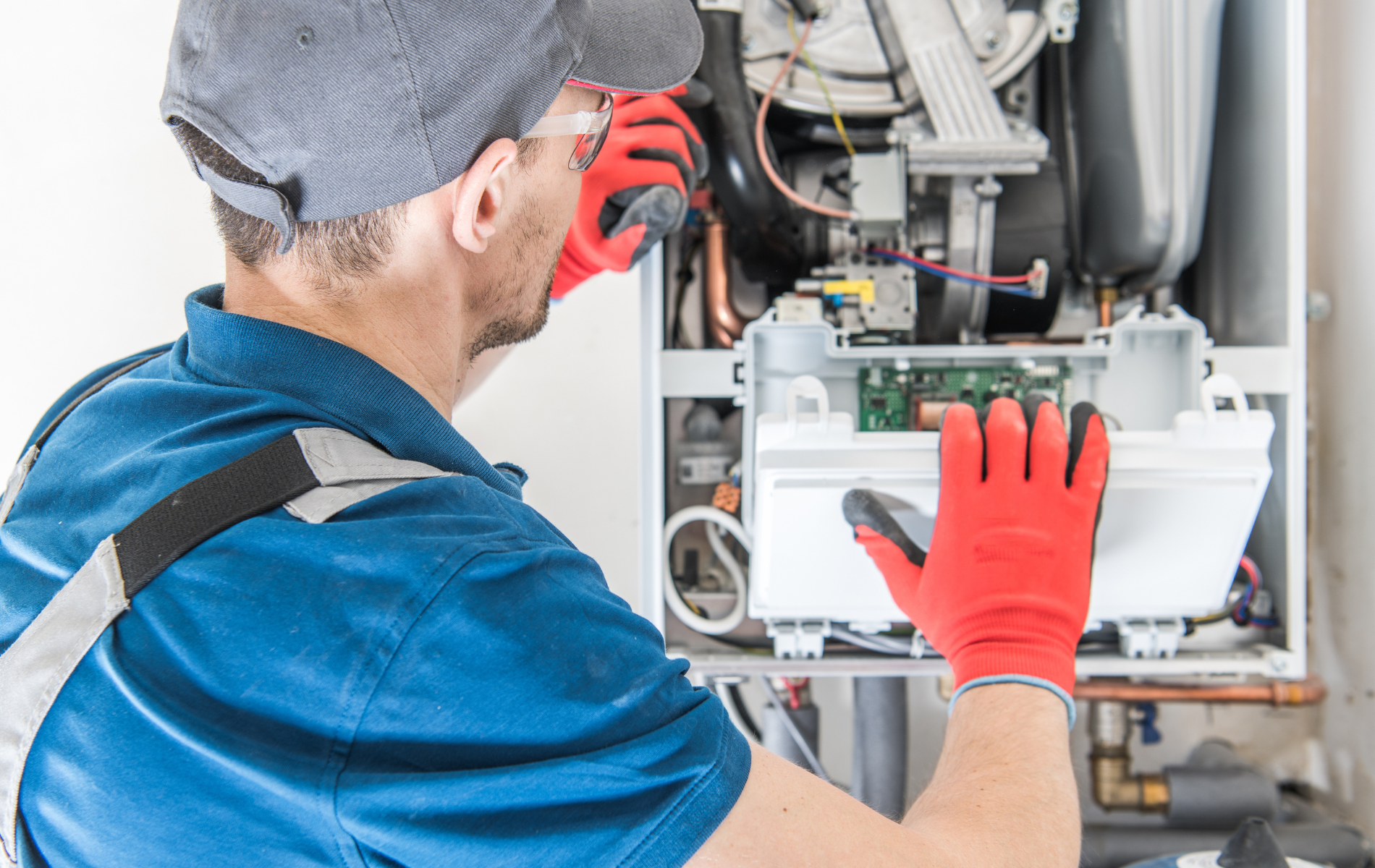 A man wearing red gloves is working on a boiler.