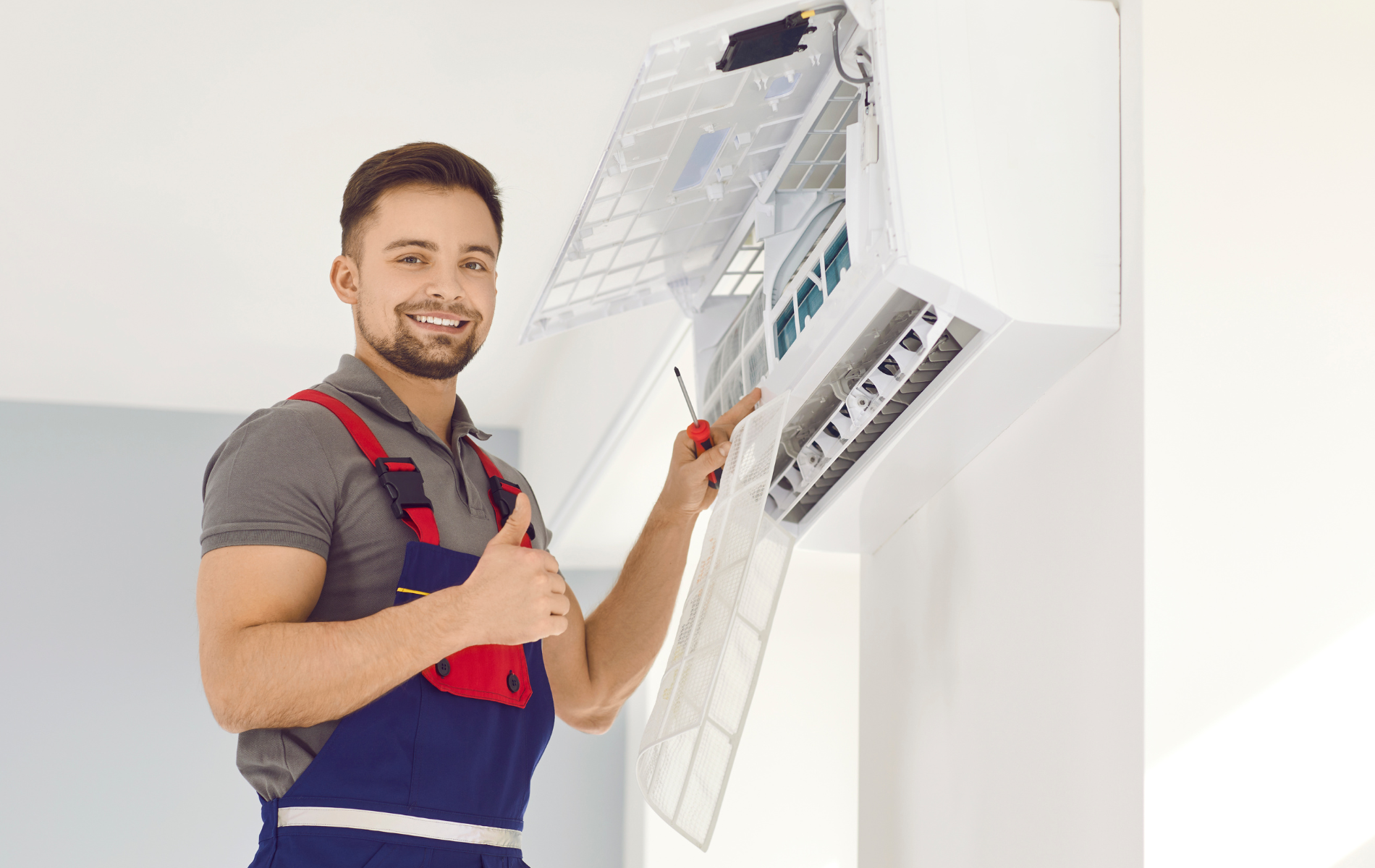 A man is fixing an air conditioner and giving a thumbs up.