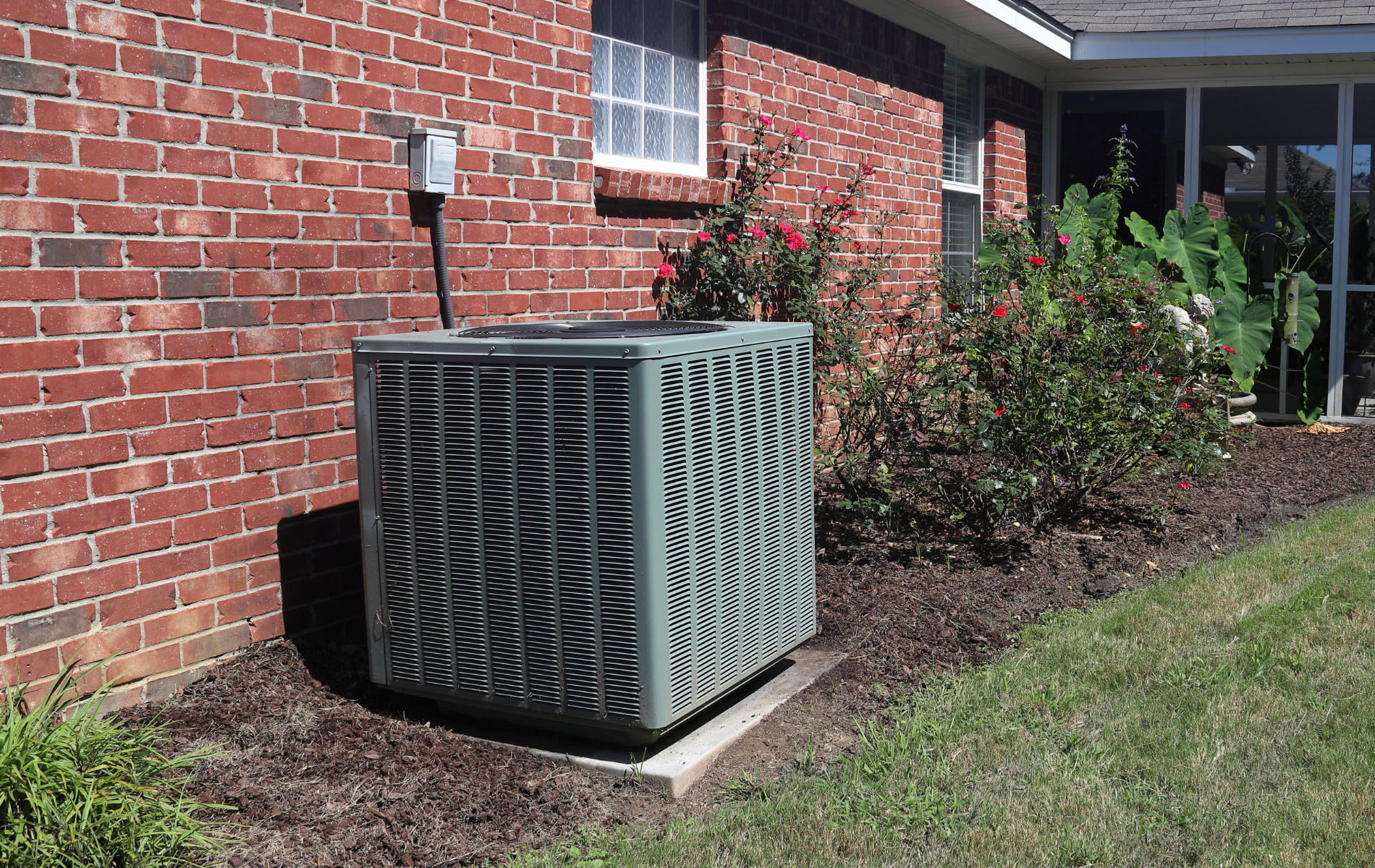 An air conditioner is sitting on the side of a brick house.