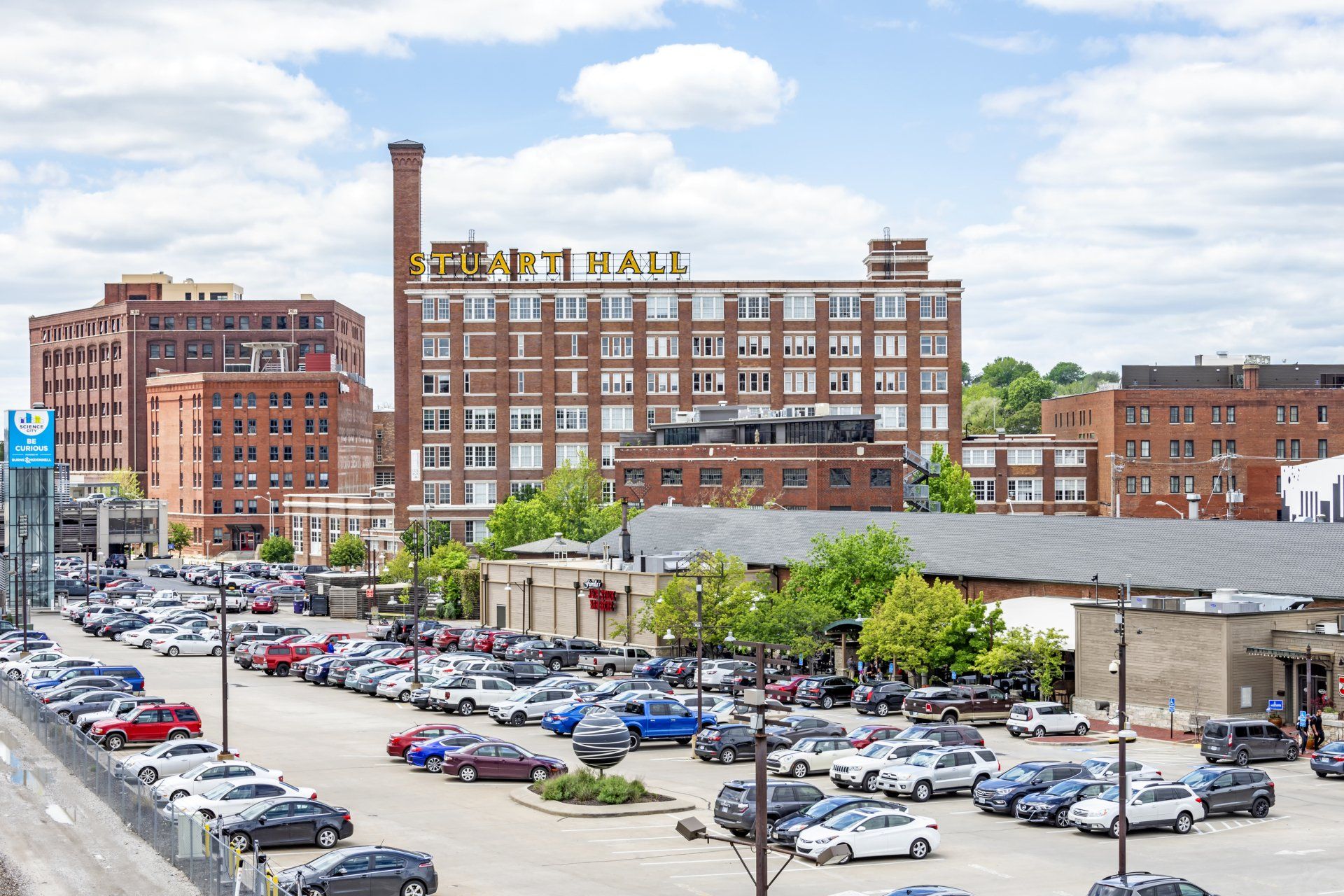A large parking lot in front of multi-story brick buildings, including one with a rooftop sign reading