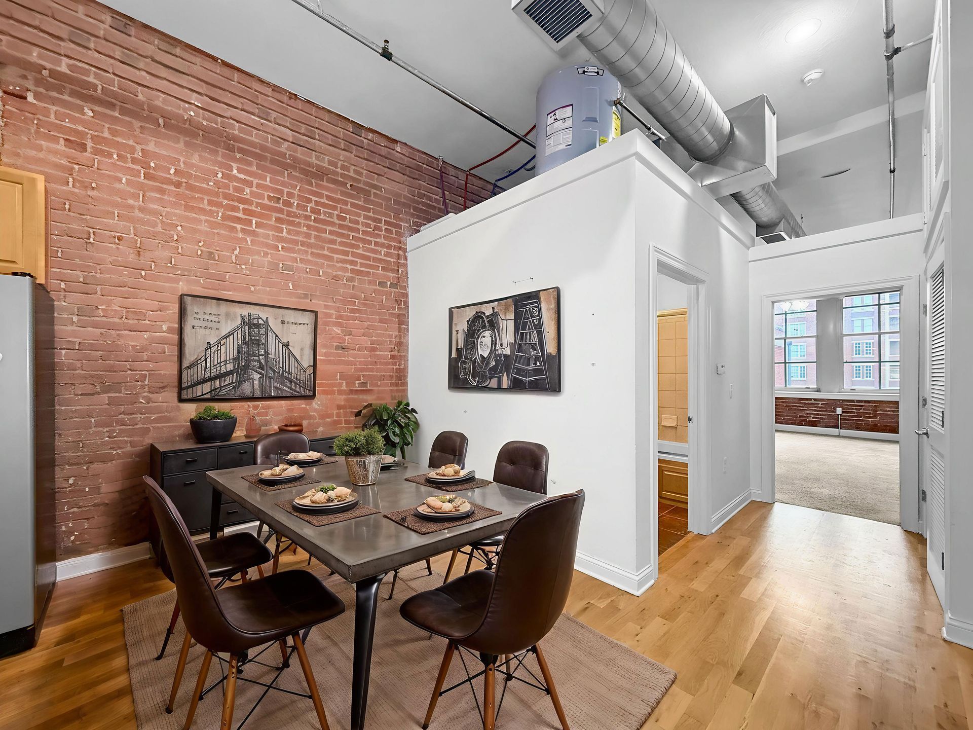 Dining area with table, chairs, exposed brick wall, and doorways in a high-ceilinged modern loft space.
