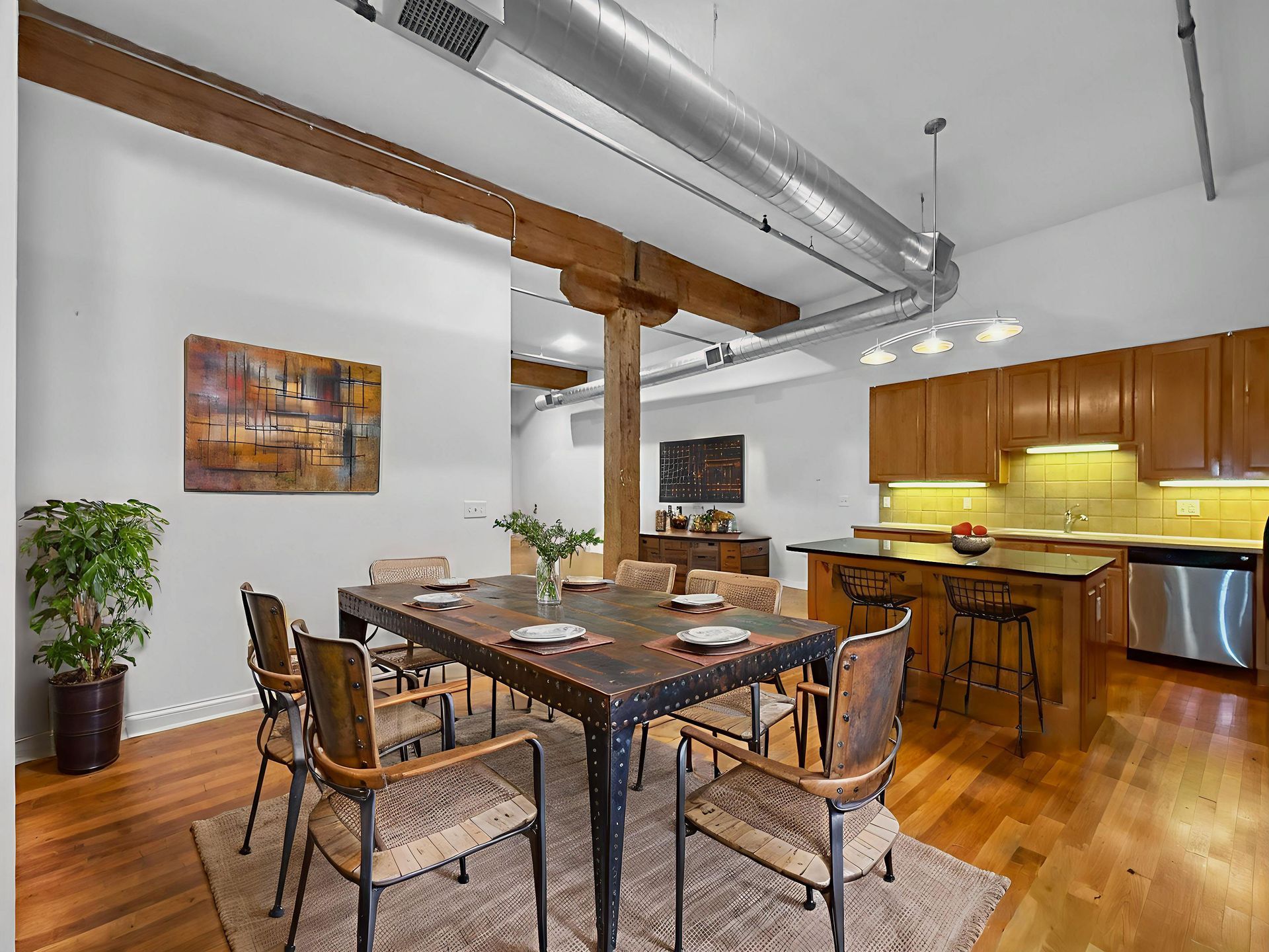 A dining area with a rustic wooden table and chairs, adjacent to a kitchen with wood cabinets and a stainless dishwasher.