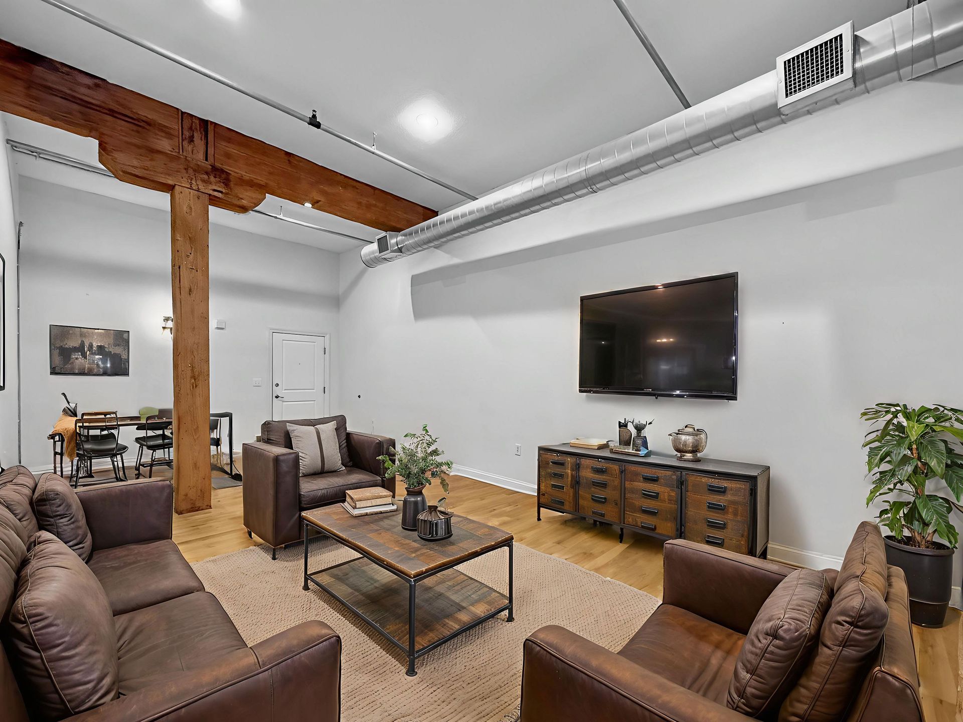 A living room with brown leather seating, a wood coffee table, a TV on the wall, and a large rustic wooden pillar.