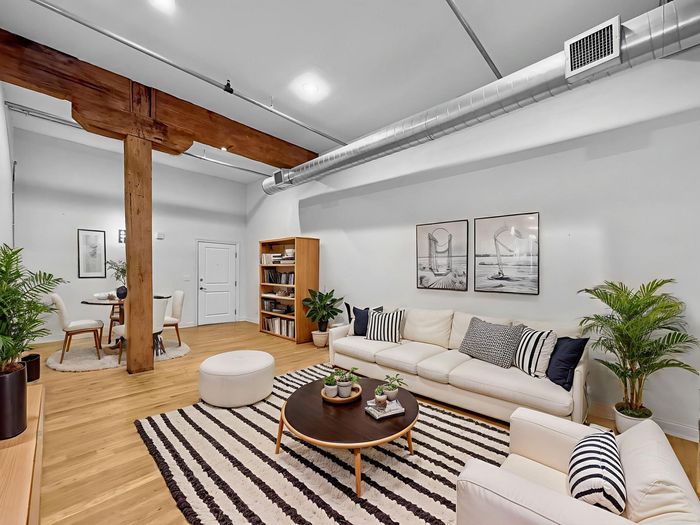Modern loft living room with a white sofa, round coffee table, striped rug, potted plants, and exposed wood pillar.