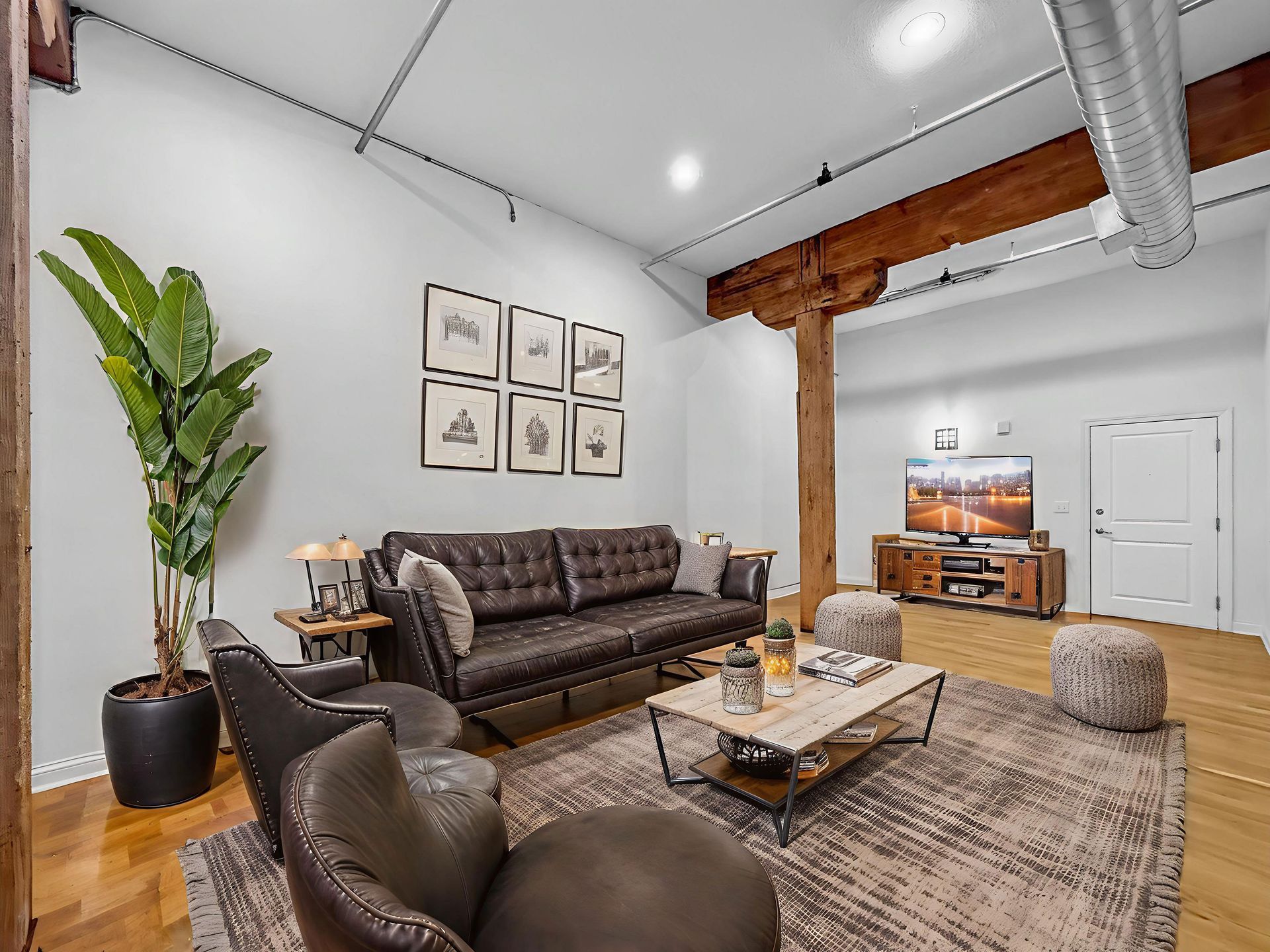 A modern living room with a brown leather sofa, matching armchair, coffee table, and large potted plant on a rug.