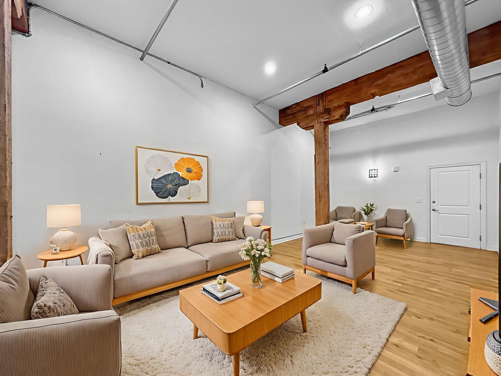 Modern industrial living room featuring a beige sofa, two armchairs, a wooden coffee table, and exposed wood beams.