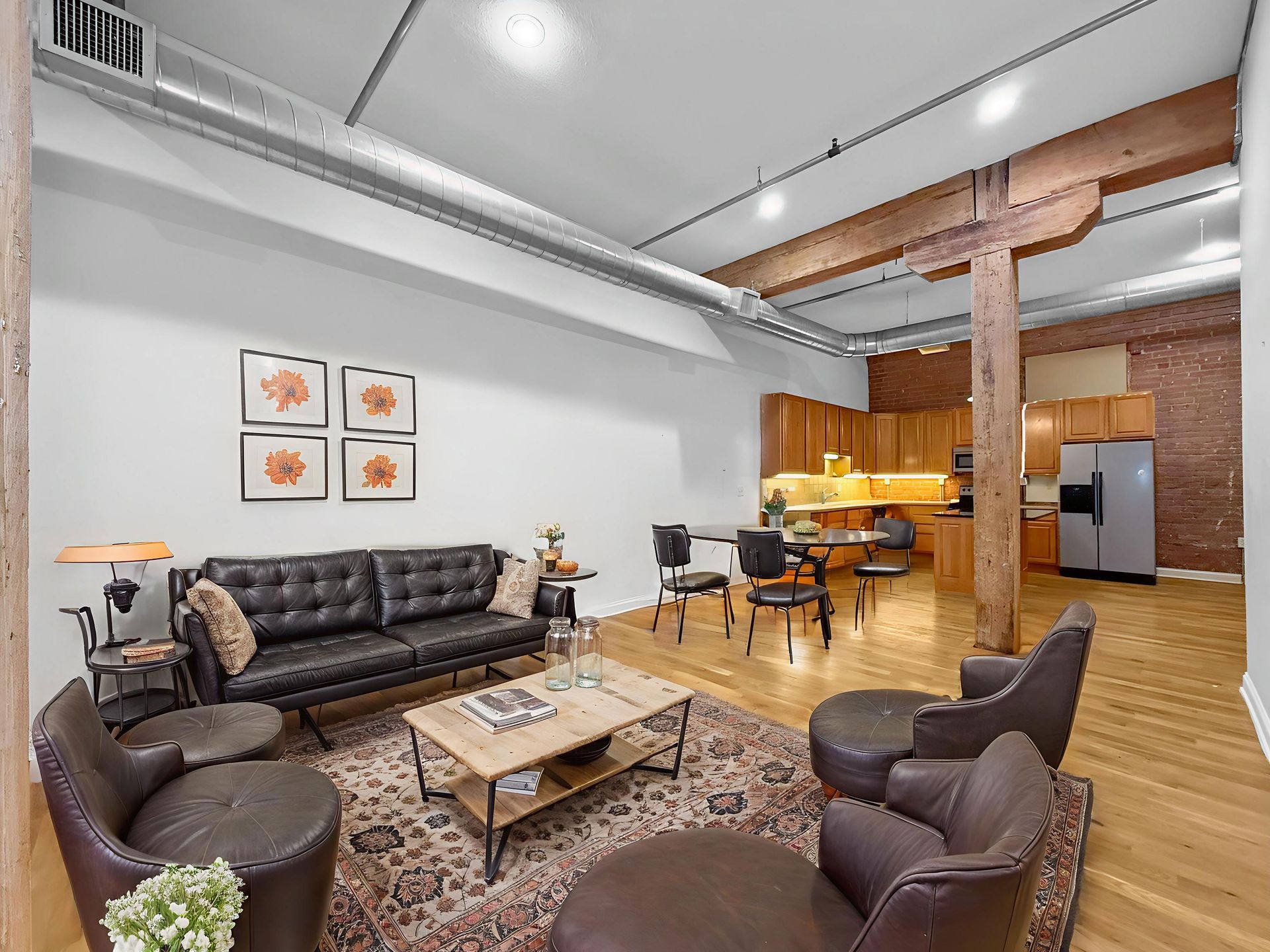 Spacious loft living room with a black tufted sofa, brown leather armchairs, coffee table, and an open kitchen background.