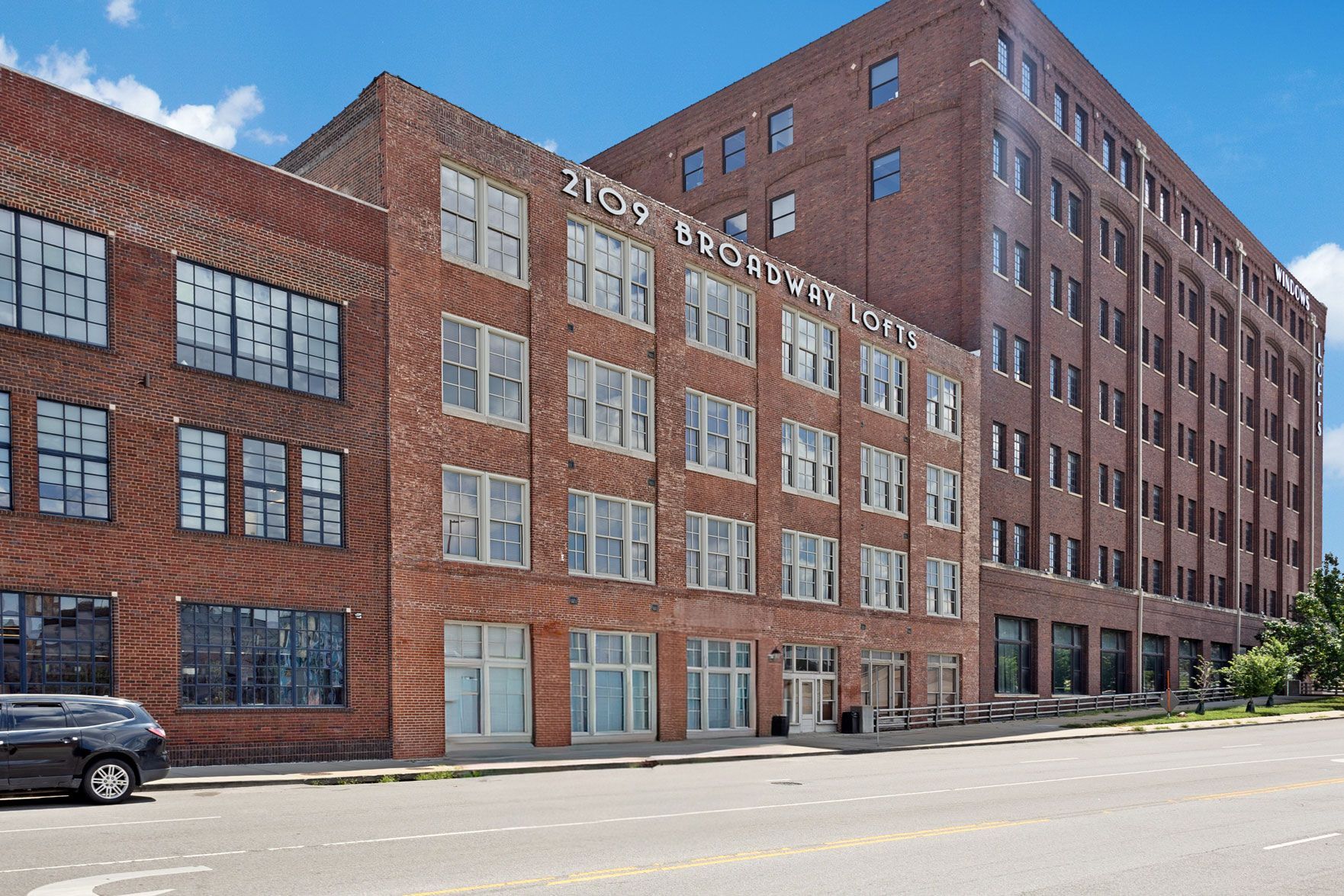 A multi-story red brick industrial building with many rectangular windows under a clear blue sky.