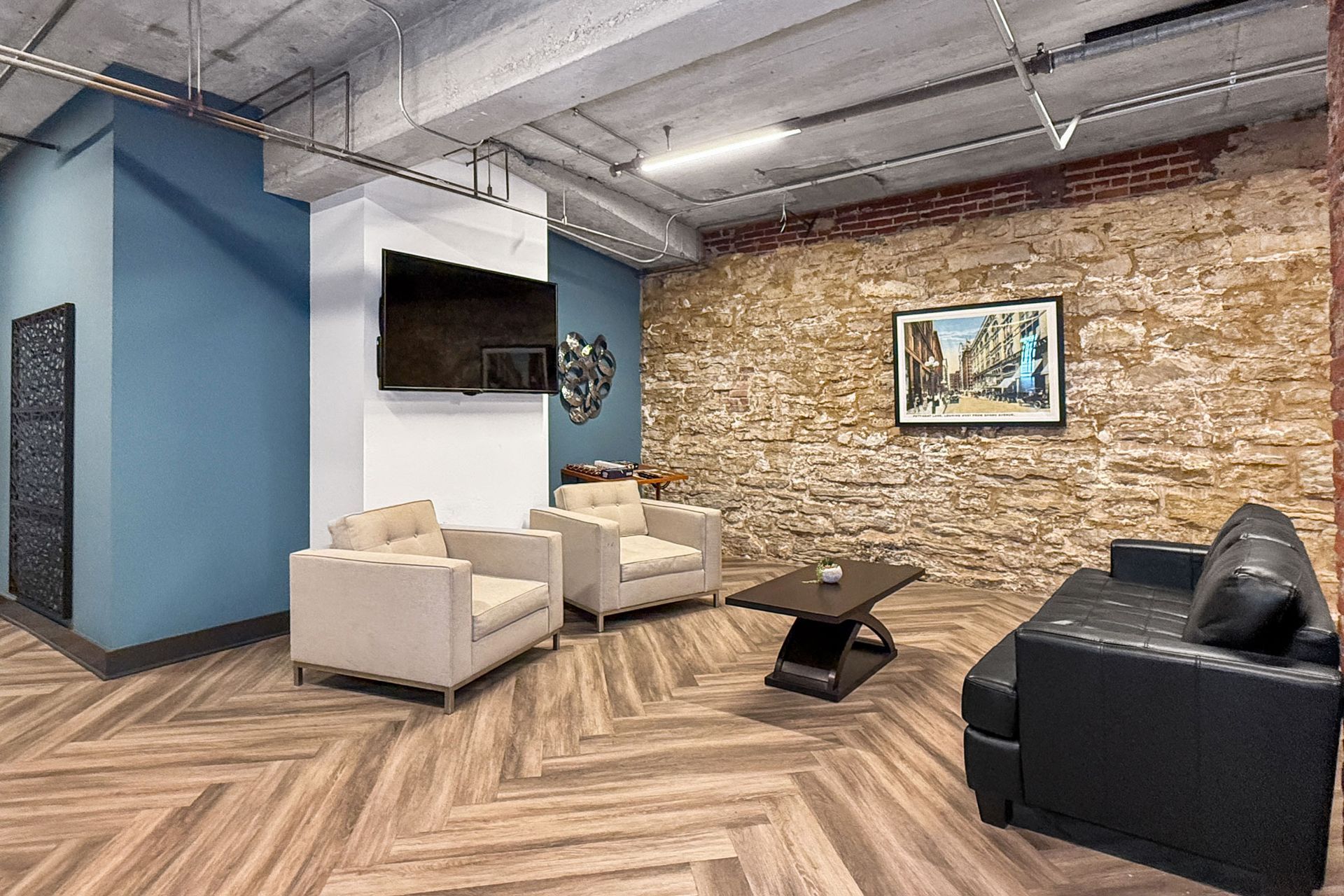 A lounge area with two beige armchairs, a black sofa, and a coffee table against a stone wall and a blue accent wall.