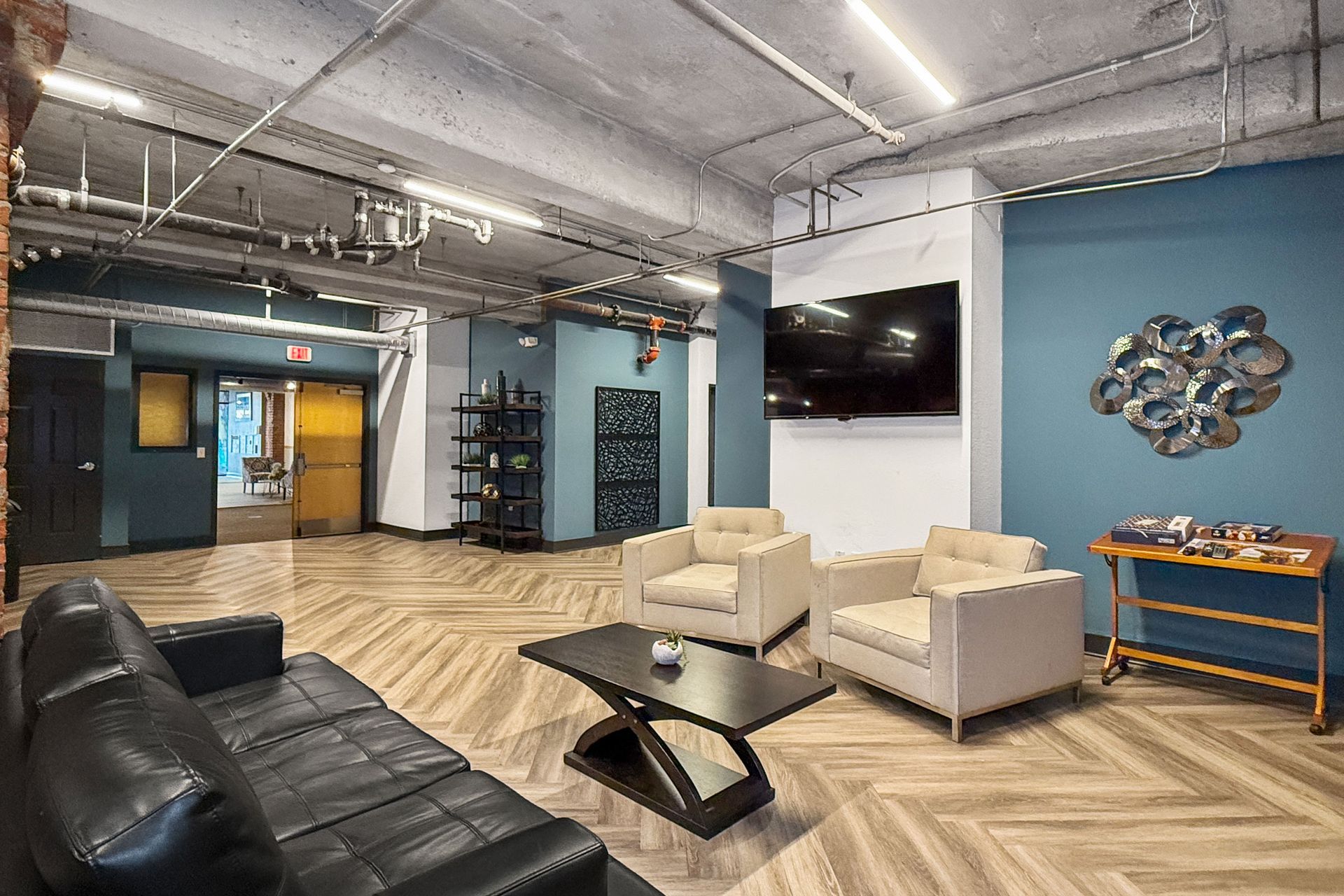 Modern lounge with a black sofa, two cream armchairs, a coffee table, a wall-mounted TV, and blue accent walls.