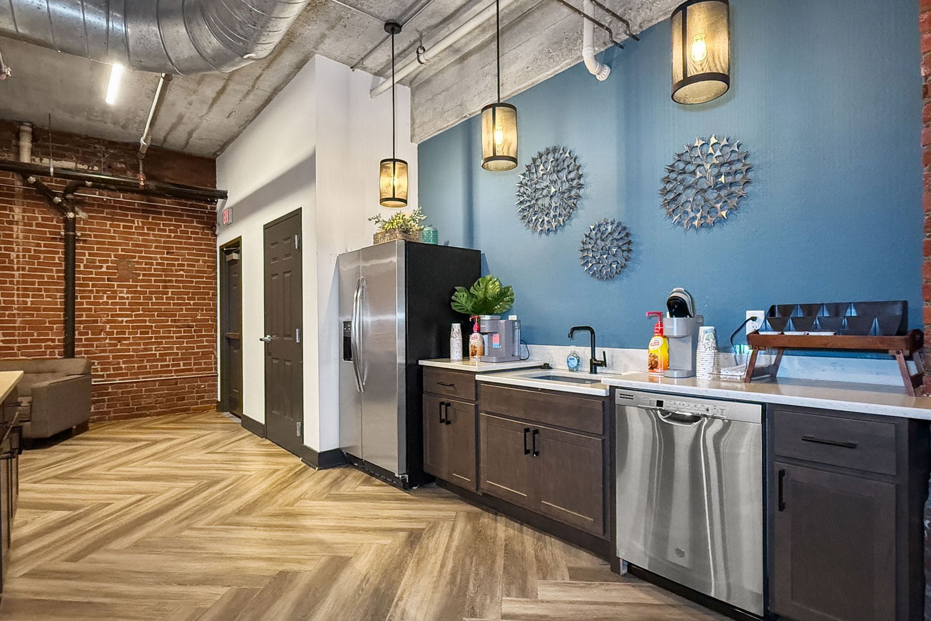 A modern breakroom with dark cabinets, stainless steel appliances, a blue wall with circular decor, and brick accents.