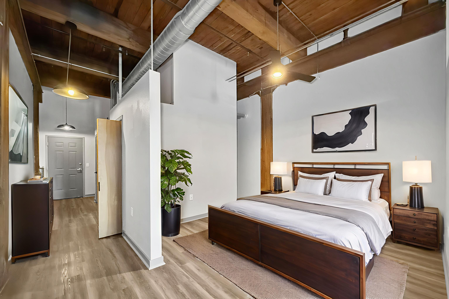 A bedroom with exposed wood ceiling beams, a dark wood bed, matching nightstands, and a privacy wall near the entryway.