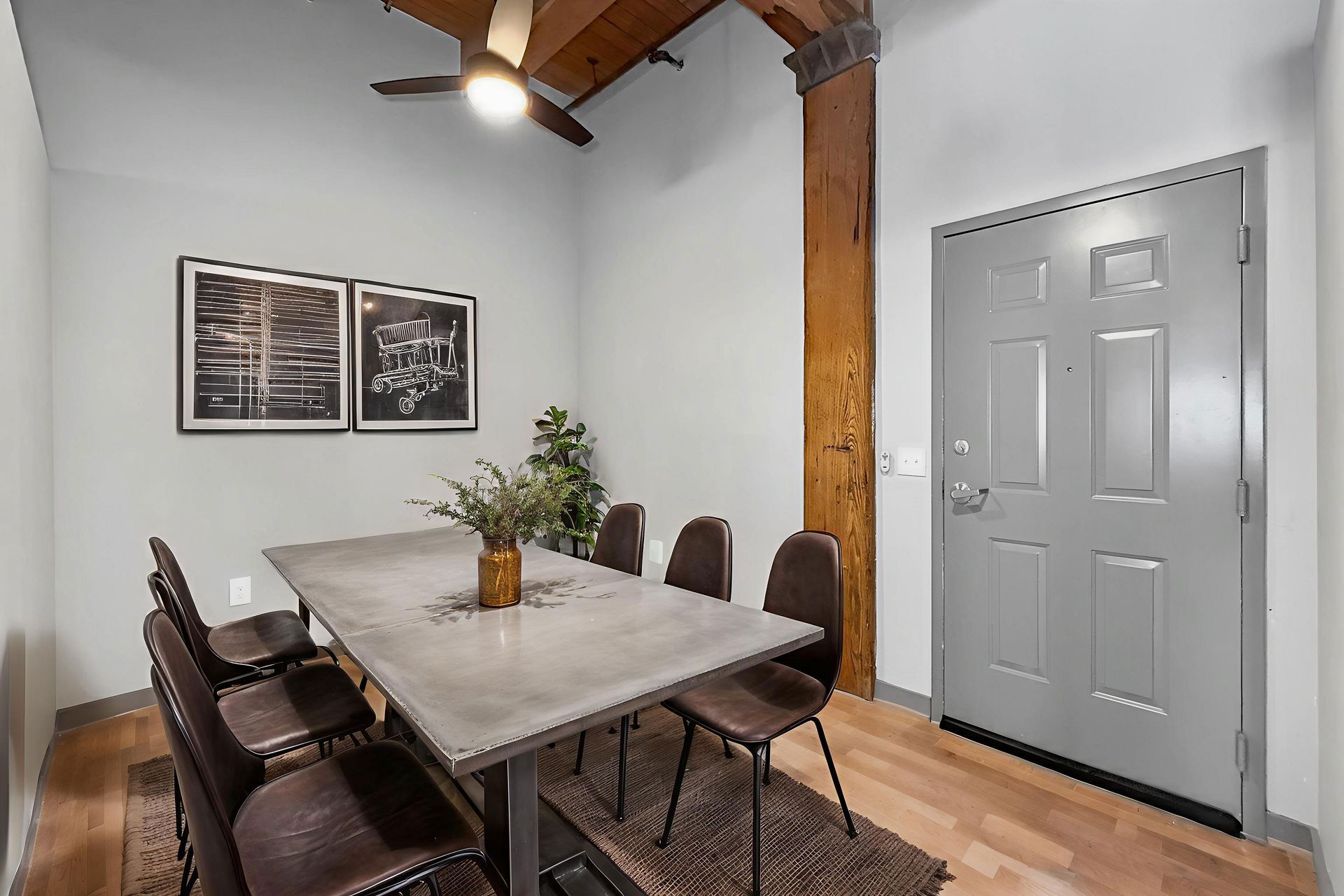A dining area with a stone table and six dark chairs on a rug in a room with a light gray door and exposed wood beam.