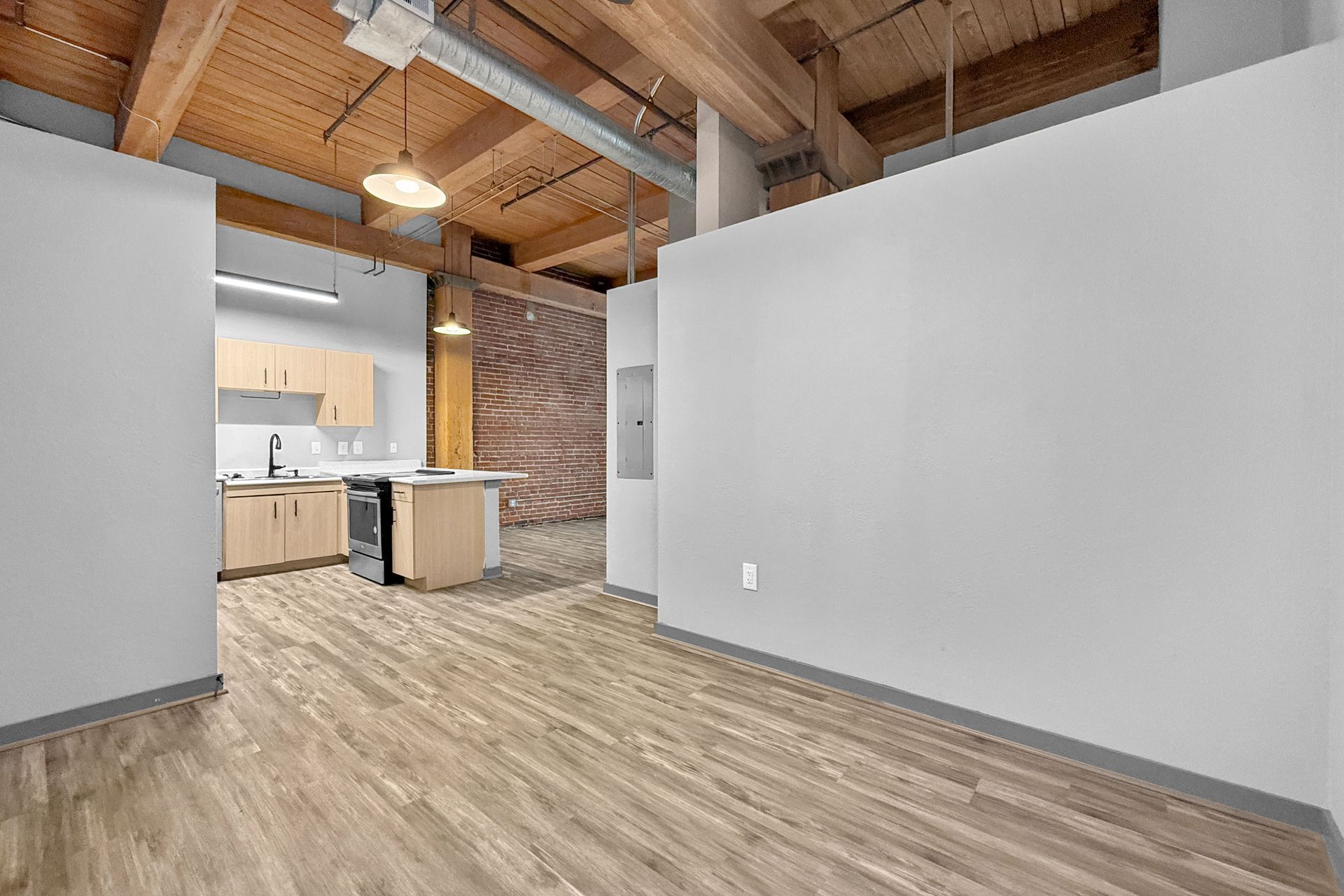 A modern studio apartment interior with wood-look floors, gray walls, open-beam ceilings, and a small, light-wood kitchen.