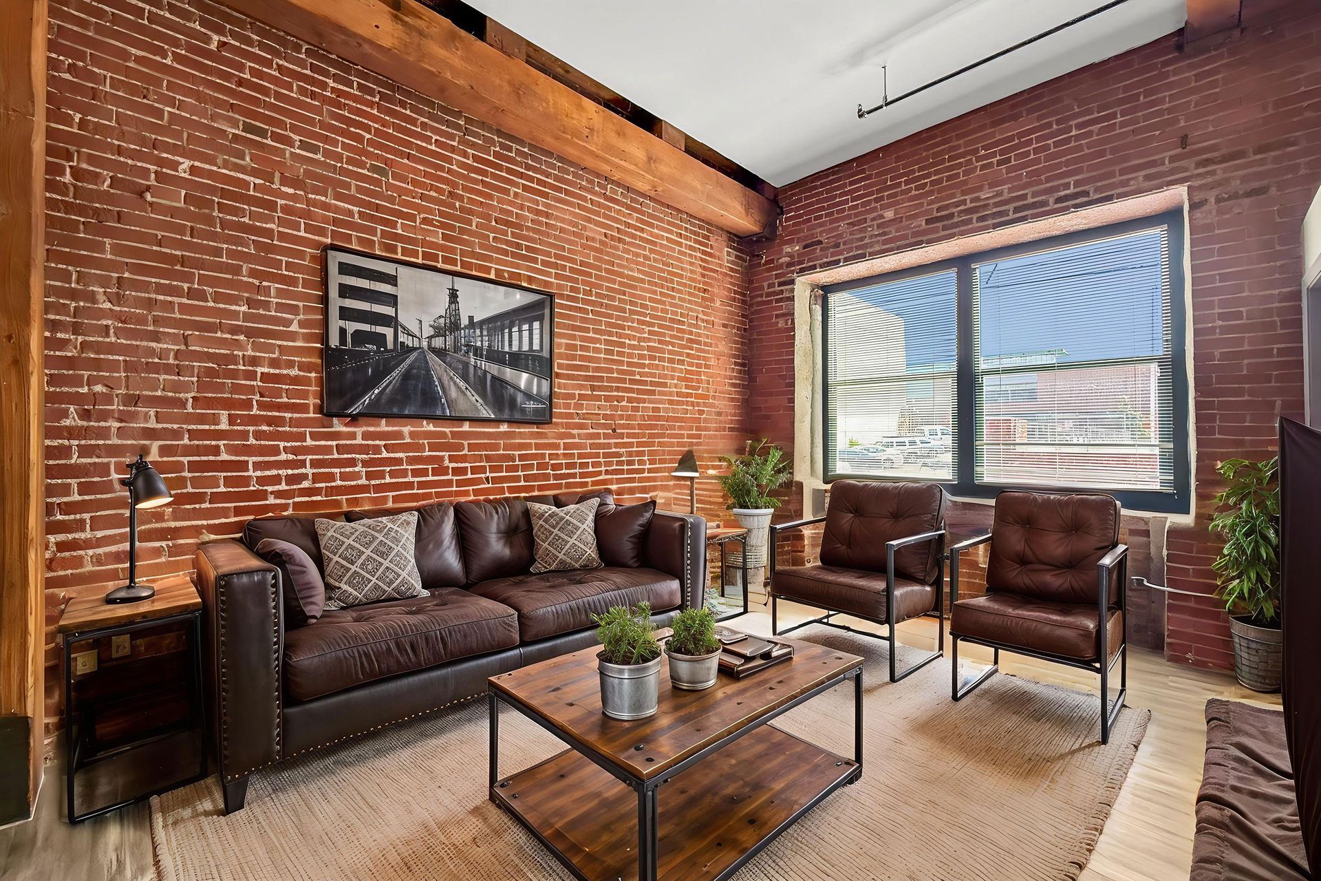 A rustic living room with exposed brick walls, a leather sofa, two leather armchairs, and a coffee table on a rug.