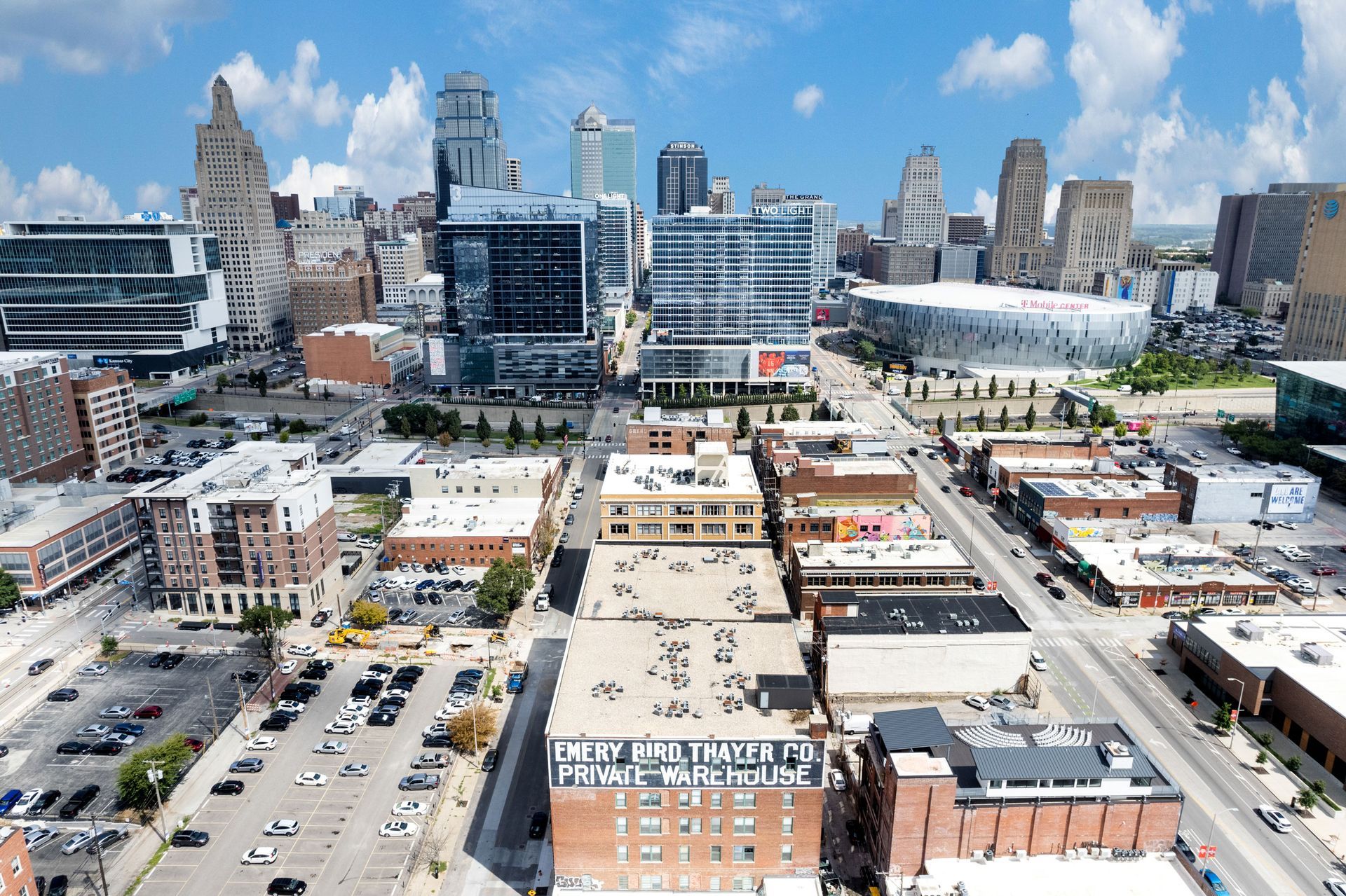 Aerial view of a city skyline with modern high-rises and commercial buildings over parking lots and urban streets.