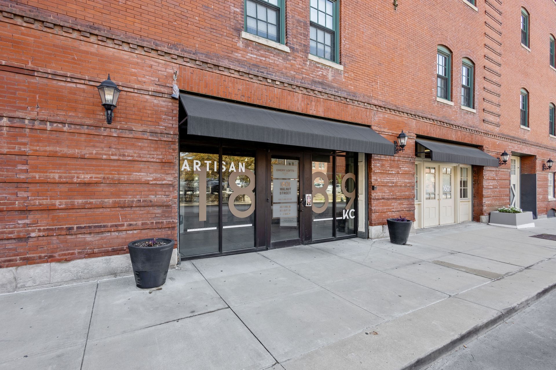 The brick storefront of Artisan 1839 with large glass windows and black awnings on a concrete sidewalk.