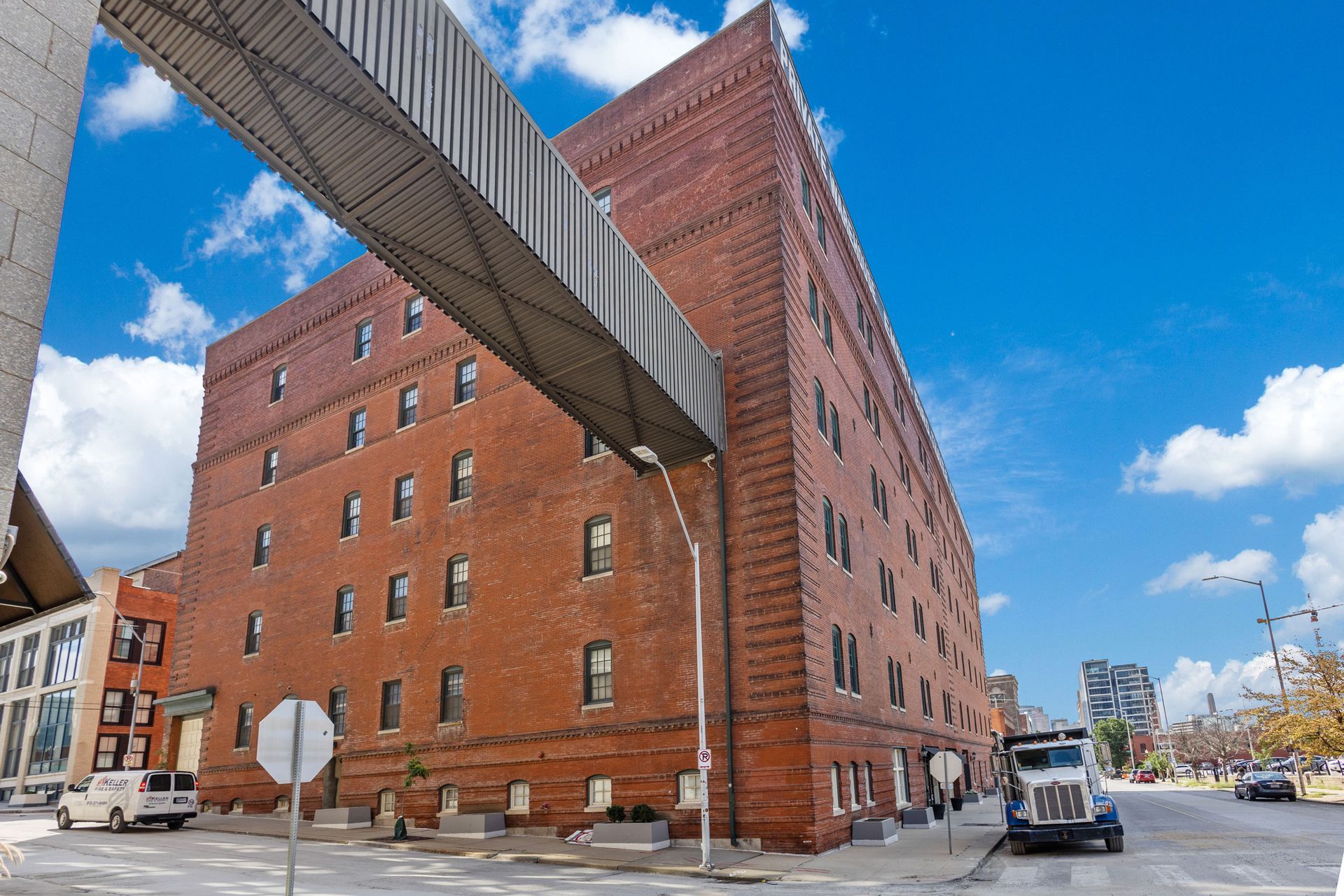 A multistory red brick building with an attached overhead walkway, under a blue sky with white clouds.