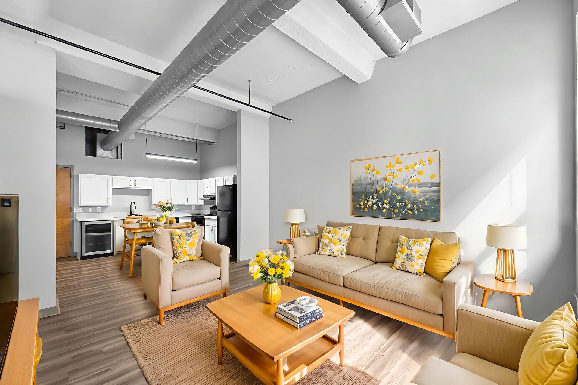 A living room with a beige sofa, two armchairs, a wooden coffee table, and an adjacent kitchen with white cabinetry.