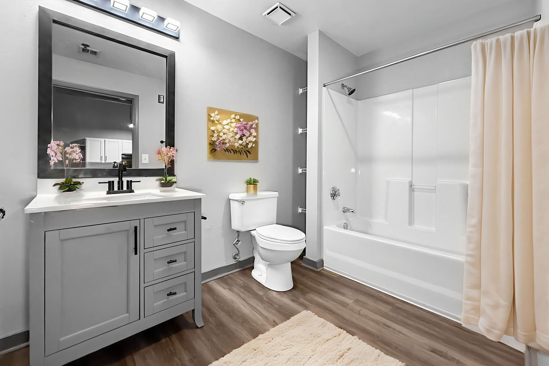 Modern bathroom with a gray vanity, white toilet, and shower-tub combination, featuring wood-look flooring.