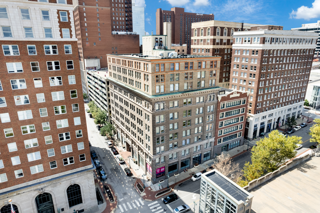 An aerial view of an urban intersection featuring several multi-story brick buildings under a bright blue sky.