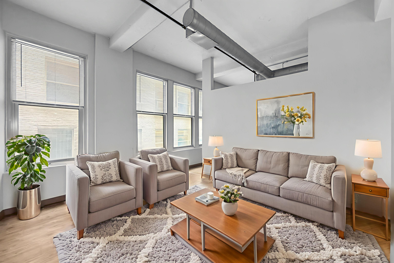 A neutral-toned living room featuring a gray sofa, two matching armchairs, a wooden coffee table, and a patterned rug.
